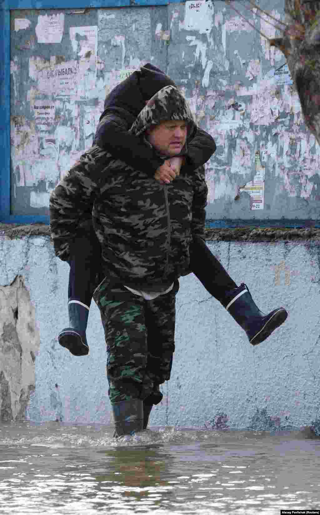 Чоловік несе на спині супутницю, йдучи затопленою вулицею в Євпаторії, яка постраждала від потужного шторму, 27 листопада 2023 року